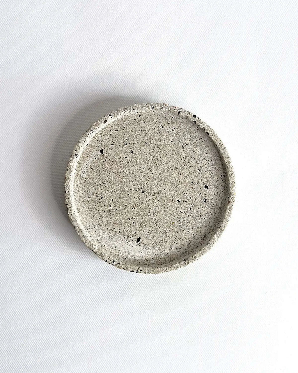 Heller, flacher Beton-Untersetzer Lura mit einem Durchmesser von 10 cm vor neutralem Hintergrund.