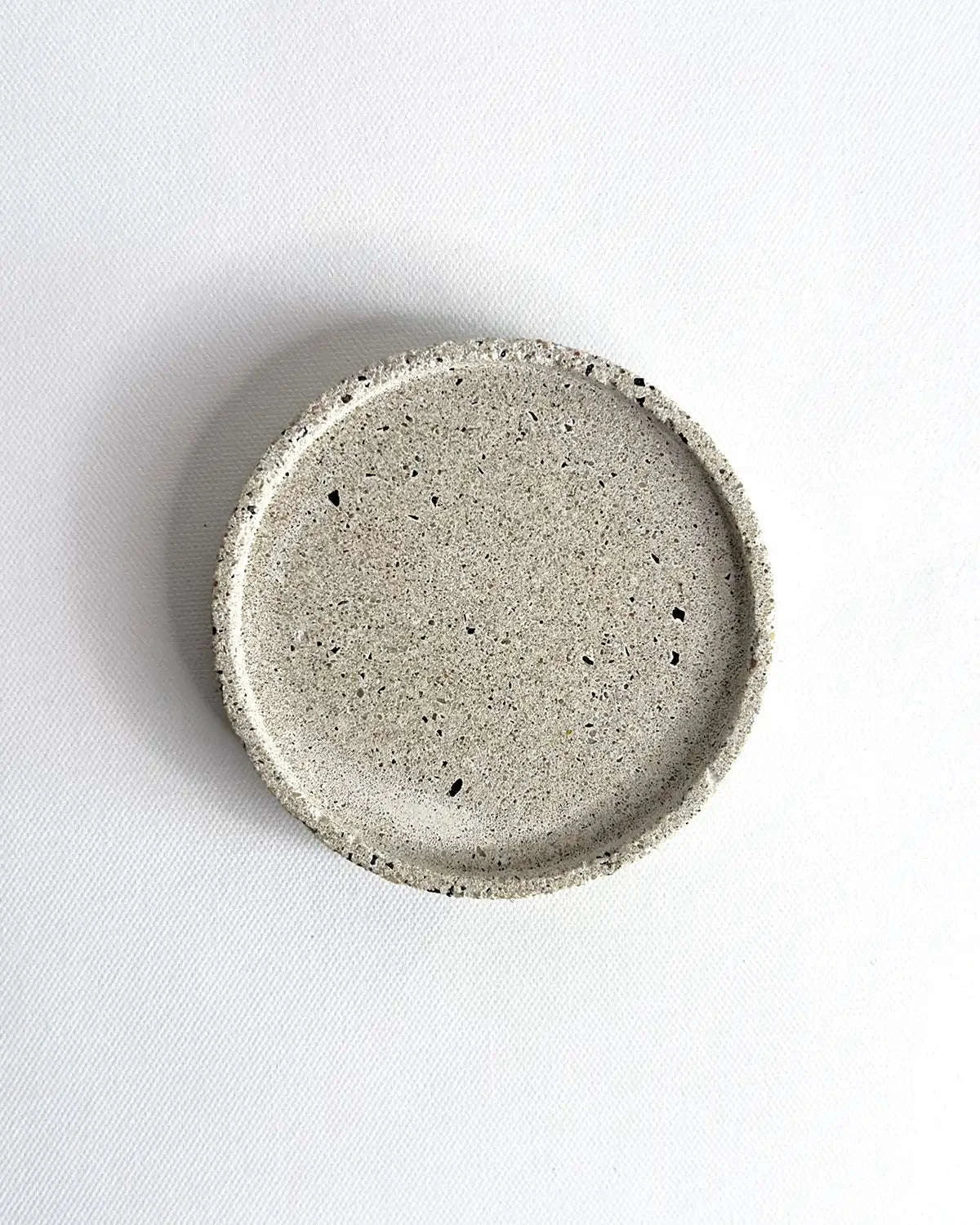 Heller, flacher Beton-Untersetzer Lura mit einem Durchmesser von 10 cm vor neutralem Hintergrund.