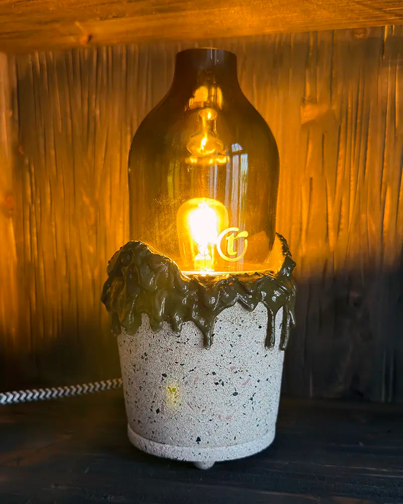 Handgefertigte Betonlampe aus einer Weinflaschen leuchtend in einem Holzregal