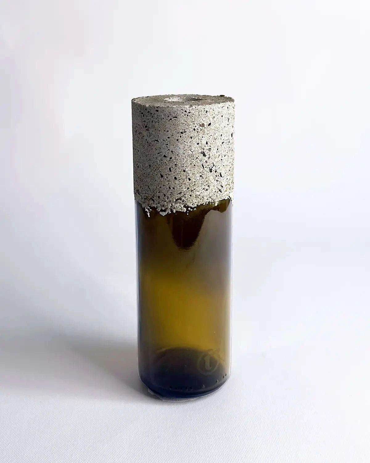 Schmale Vase aus braunem Upcycling-Glas mit grober Betonmanschette vor hellem Hintergrund