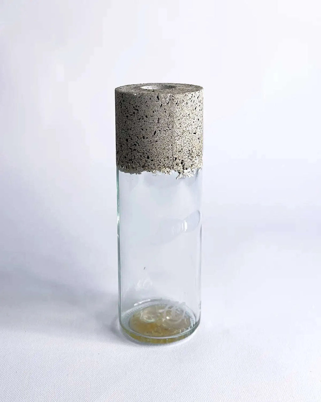 Schmale Vase aus klarem Upcycling-Glas mit grober Betonmanschette vor hellem Hintergrund