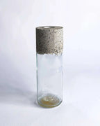 Schmale Vase aus klarem Upcycling-Glas mit grober Betonmanschette vor hellem Hintergrund