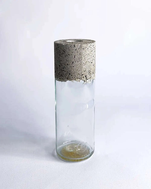 Schmale Vase aus klarem Upcycling-Glas mit grober Betonmanschette vor hellem Hintergrund