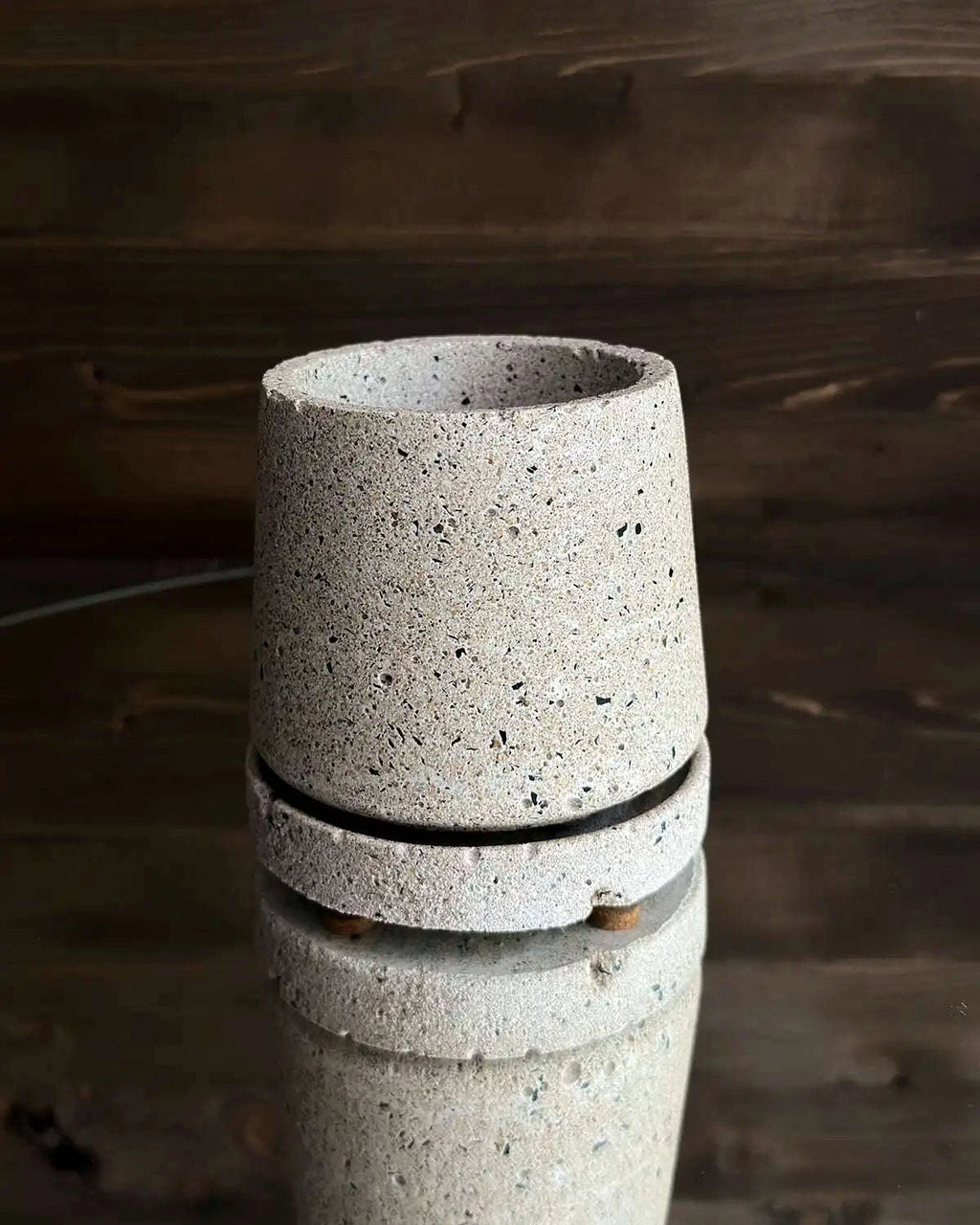 Pflanzgefäß aus hellem Beton mit passendem Untersetzer vor dunkler Holzwand
