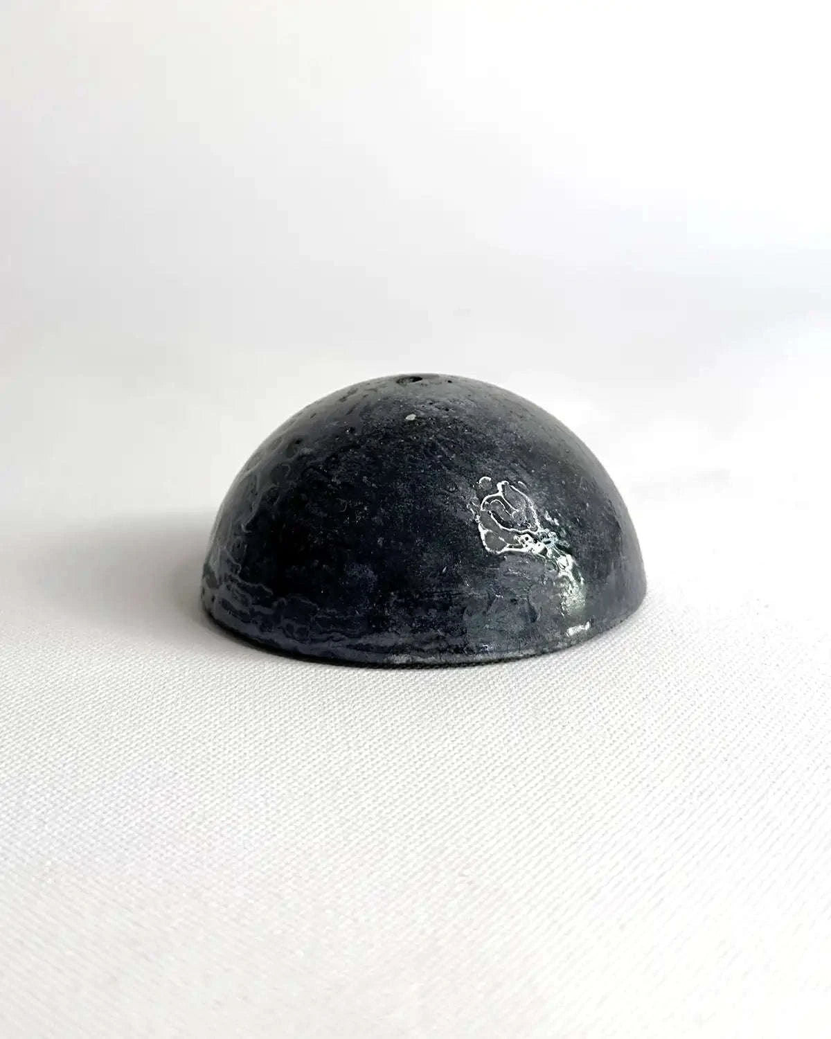 Halbkugelförmiges Betonobjekt in Schwarz vor hellem Hintergrund.