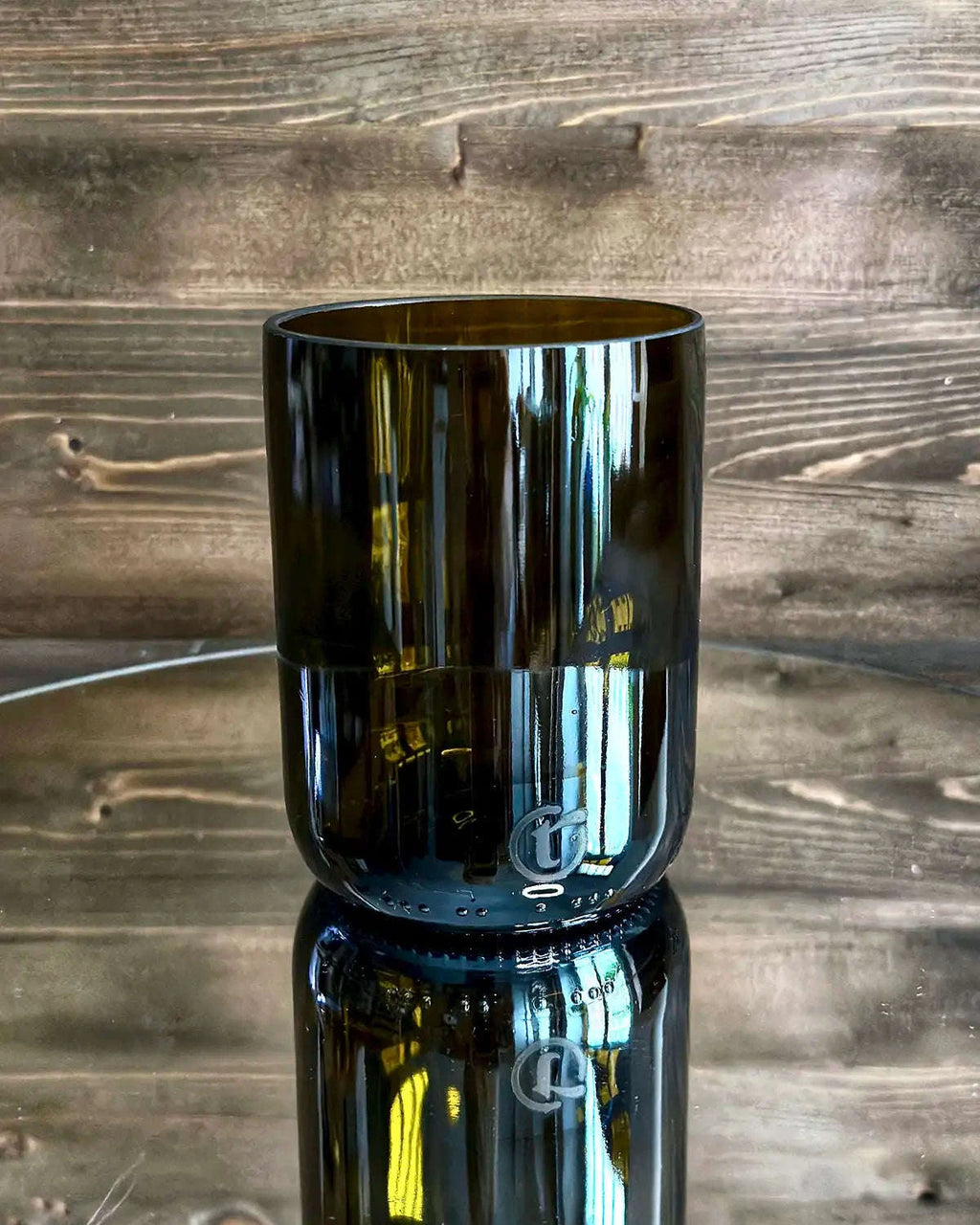 Trinkglas aus antikgrünem Upcycling-Glas auf Spiegelplatte vor dunkler Holzwand