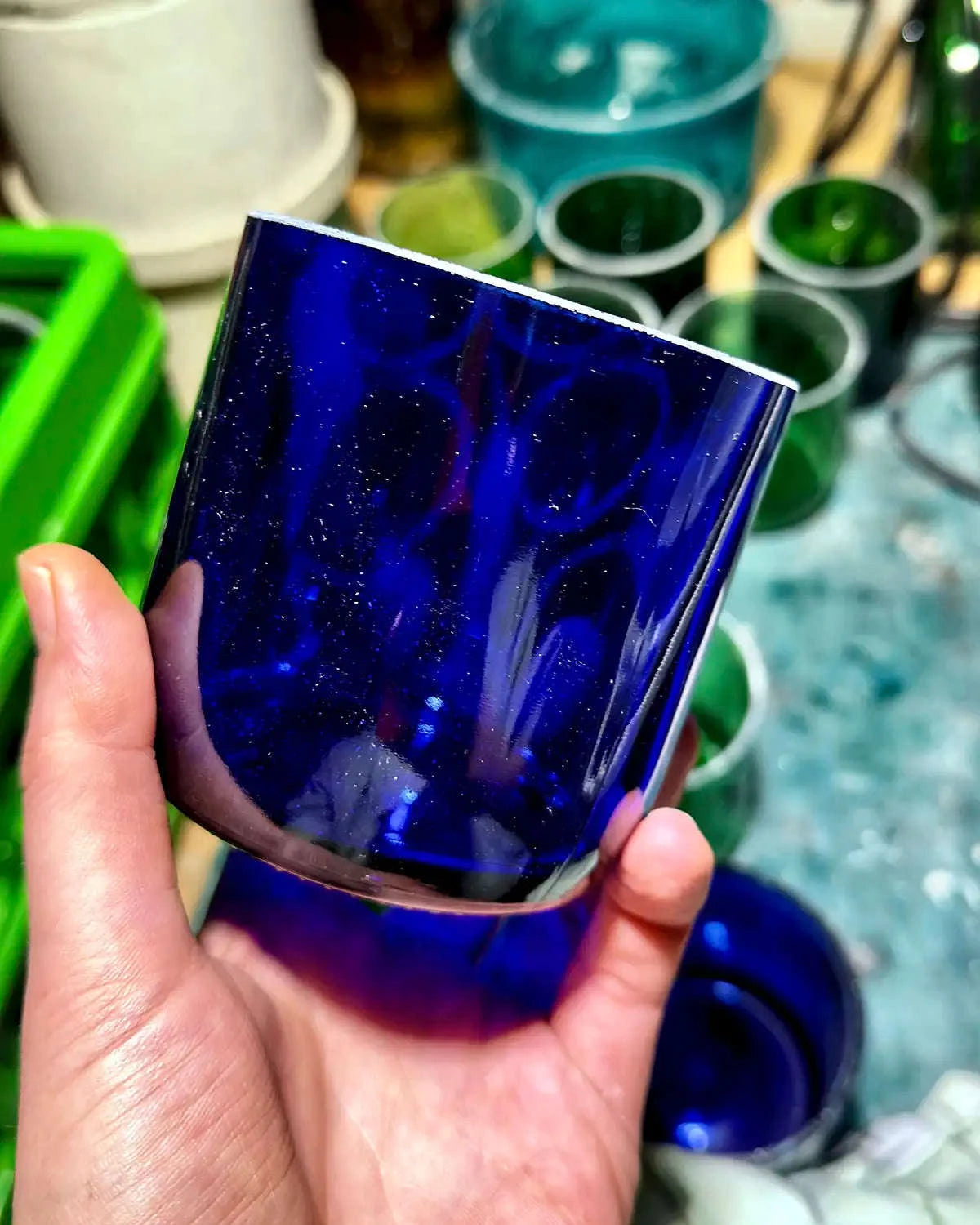 Blaues Glas in der Hand vor Werkbank mit weiteren zugeschnittenen Glasstücken