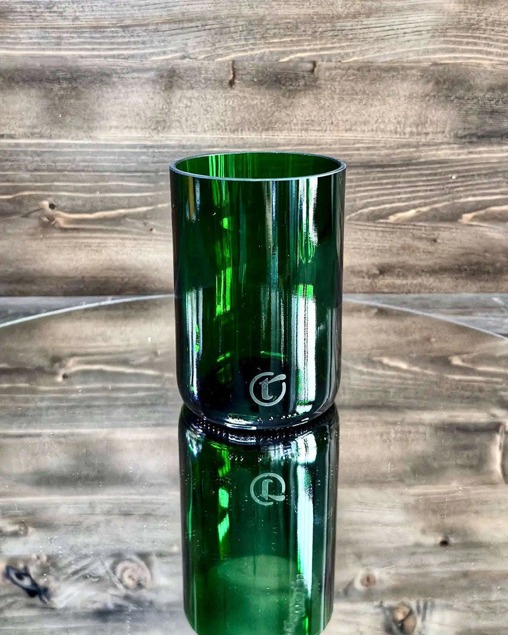Dunkelgrünes Upcycling-Glas auf Spiegelplatte vor dunkler Holzwand