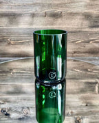 Dunkelgrünes Upcycling-Glas auf Spiegelplatte vor dunkler Holzwand