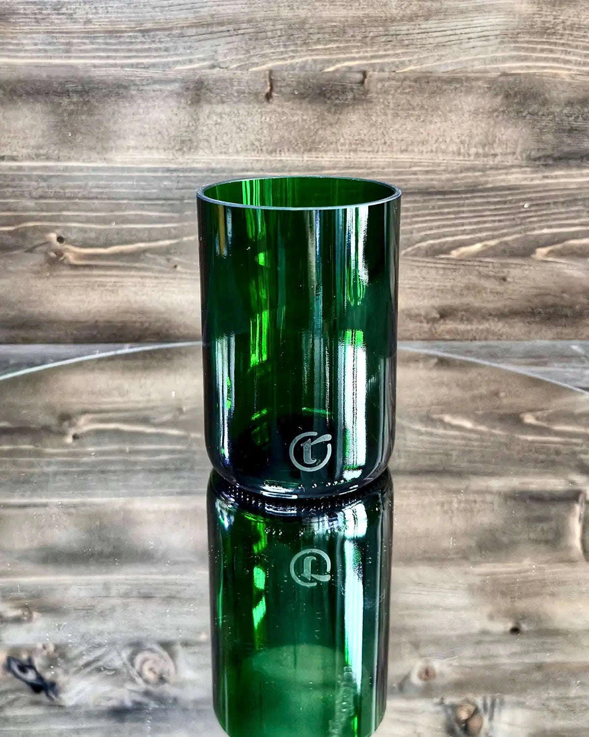 Dunkelgrünes Upcycling-Glas auf Spiegelplatte vor dunkler Holzwand
