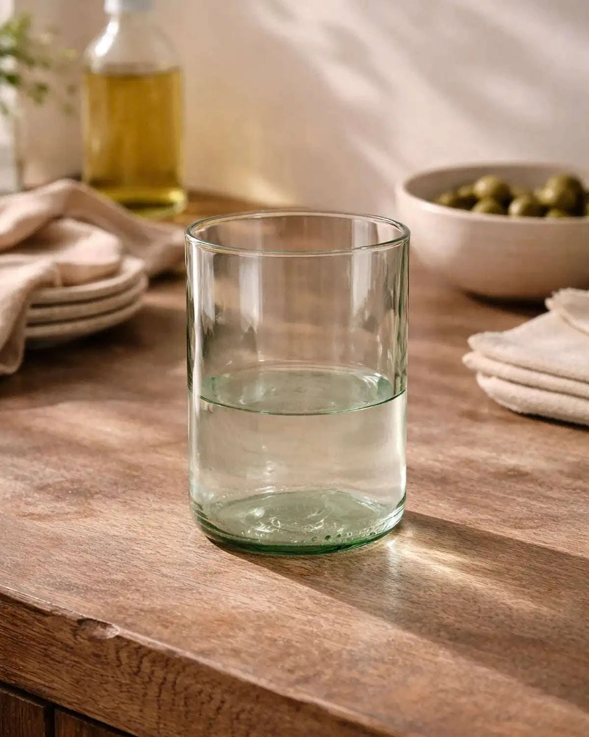 Klares Wasserglas auf Holztisch mit Wasser in heller Küchenszene mit Tellern und Schale