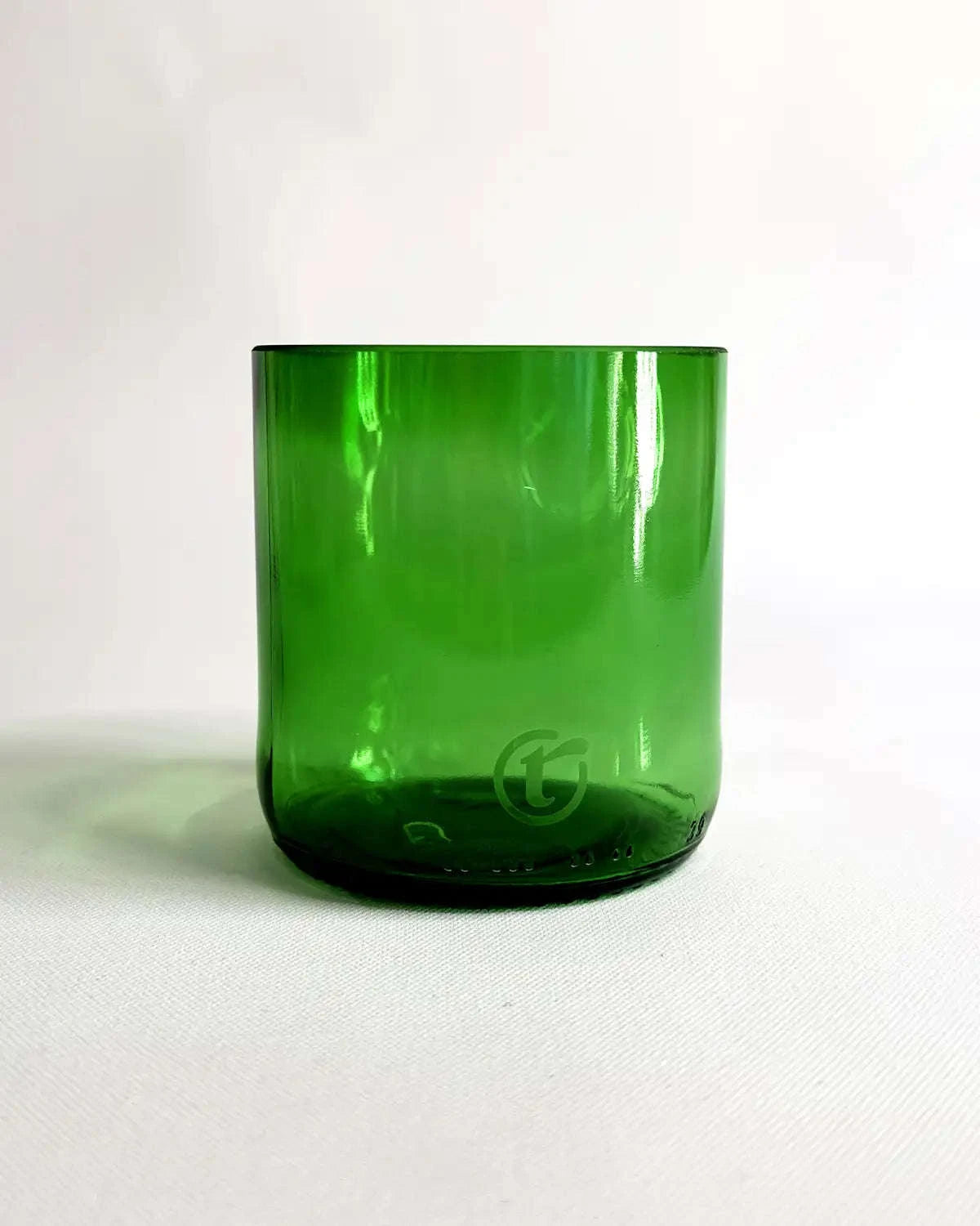 Grünes handgefertigtes Glas als Freisteller auf hellem Stoff.