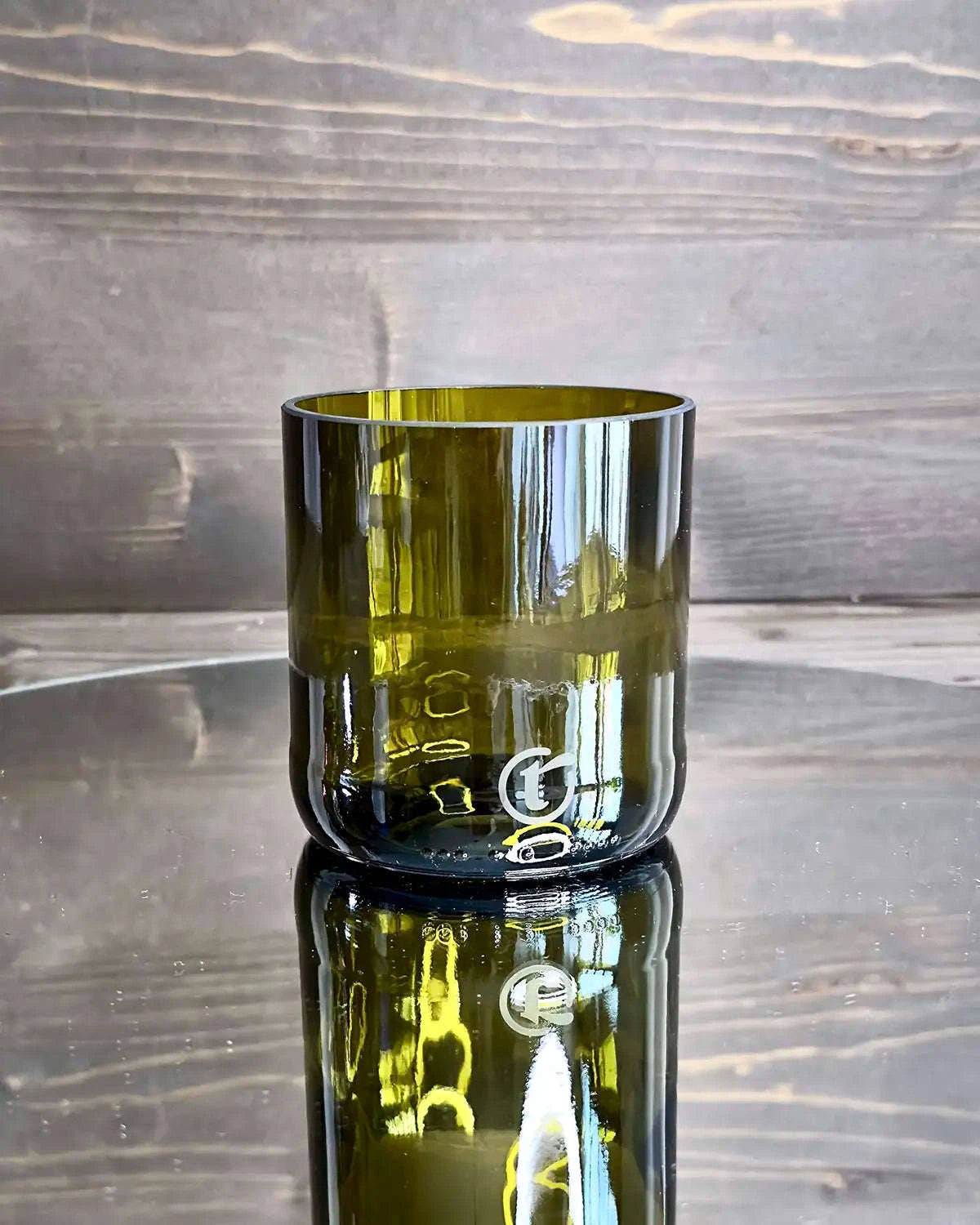 Kleines braungrünes handgemachtes Glas aus recyceltem Flaschenglas platziert auf einem Spiegel.