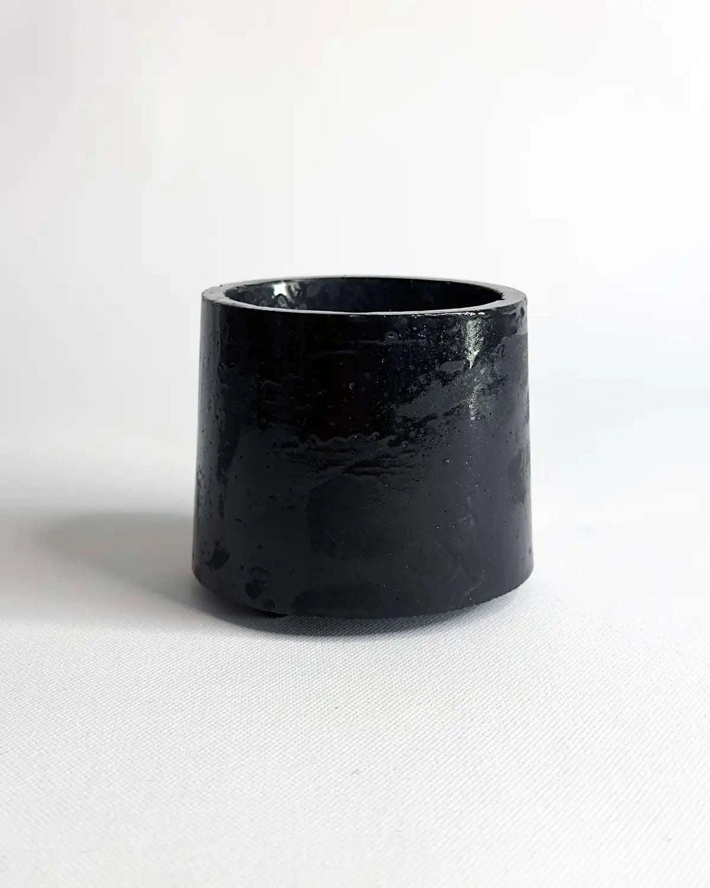 Schwarzer Mini Pflanztopf aus Beton vor hellem Hintergrund.