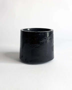 Schwarzer Mini Pflanztopf aus Beton vor hellem Hintergrund.