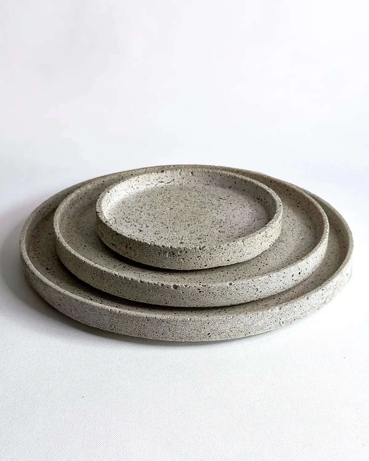 Mehrere flache, runde Dekoteller Petela aus hellem Beton übereinandergestapelt.