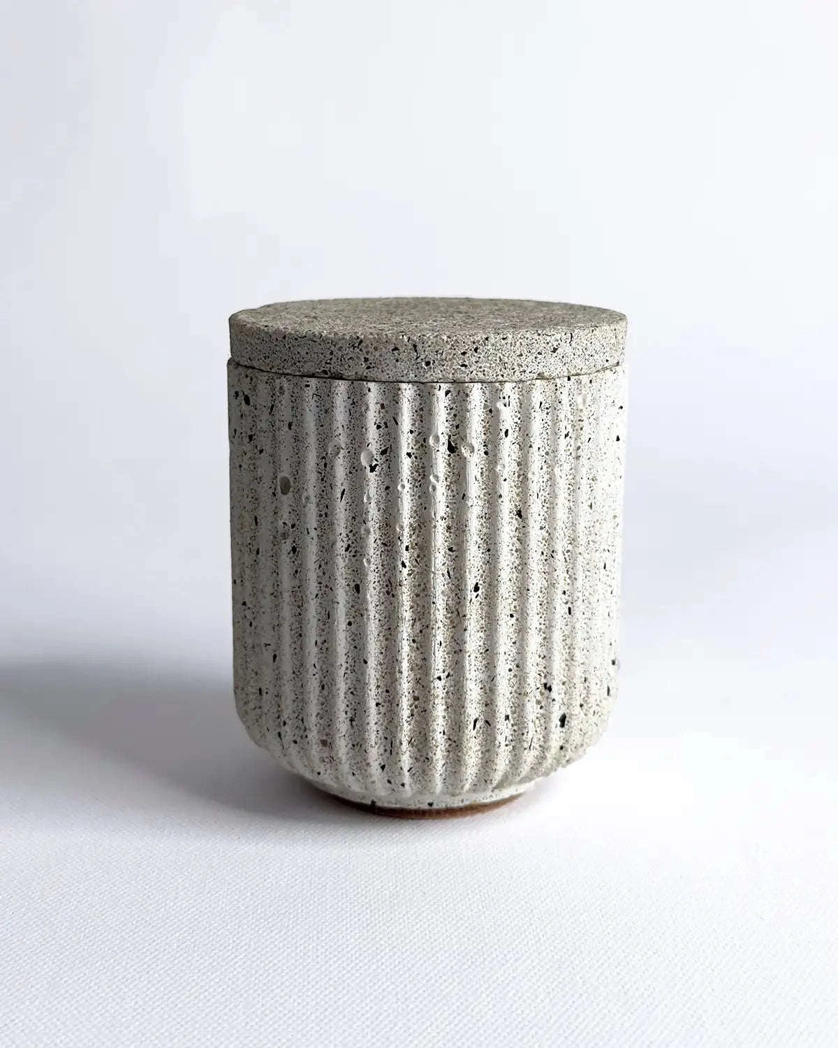 Aufbewahrungsbehälter aus Beton mit passendem Deckel in geriffelter Form.
