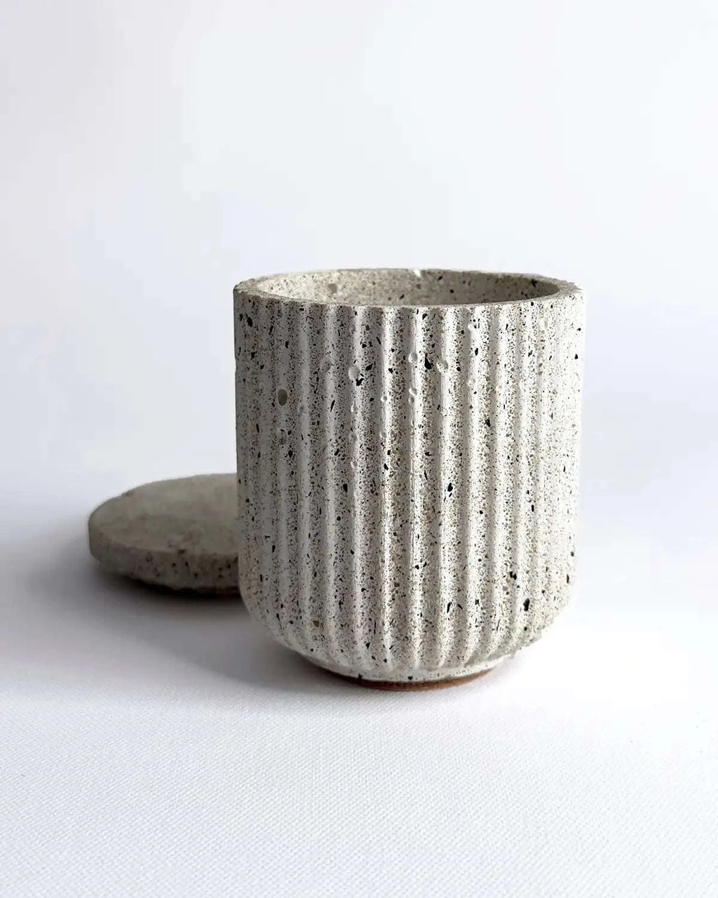 Minimalistisches Betongefäß mit feiner Rillenstruktur und abgenommenem Deckel.