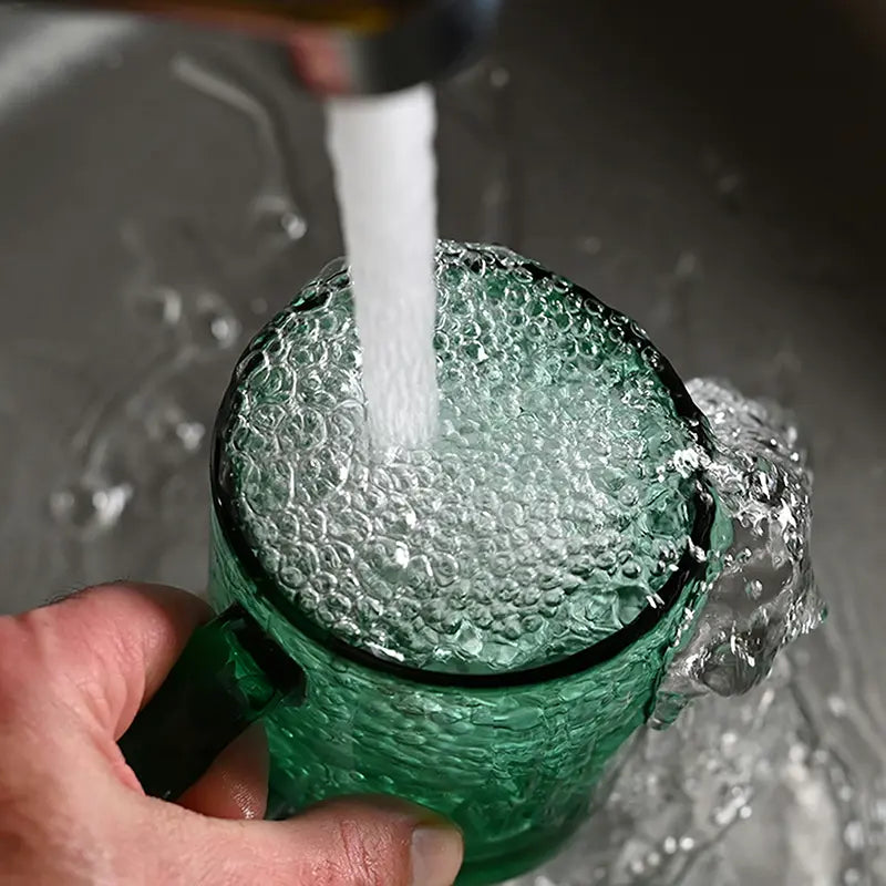 Grünes Trinkglas aus einer upgecycelten Weinflasche wird unter fließendem Wasser gereinigt.