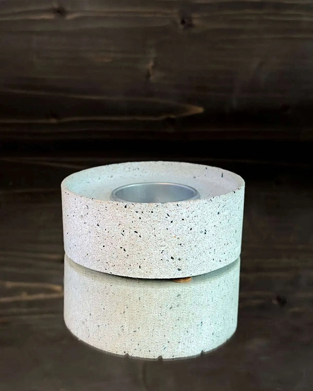 Runder Betonsockel für Windlicht mit eingesetztem Metall-Teelichthalter auf Spiegelplatte.