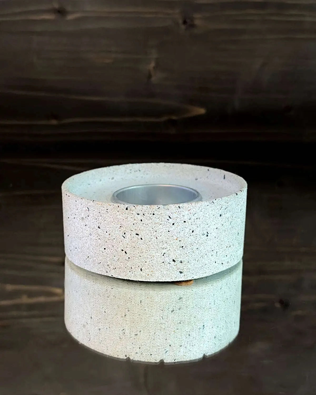 Runder Betonsockel für Windlicht mit eingesetztem Metall-Teelichthalter auf Spiegelplatte.