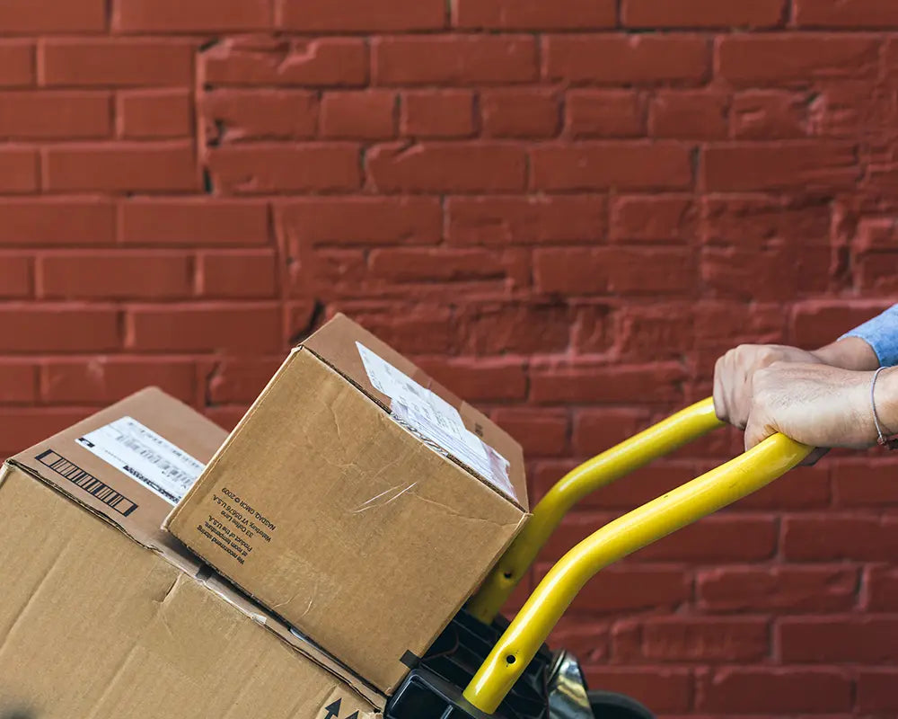 Versandkartons auf einer Sackkarre vor roter Backsteinwand als Motiv für Lieferung und Paketversand bei tian