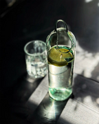 Glaskaraffe mit tropfenförmigem Ausguss aus einer geschliffenen Weinflasche mit Zitronenwasser und passendem Wasserglas