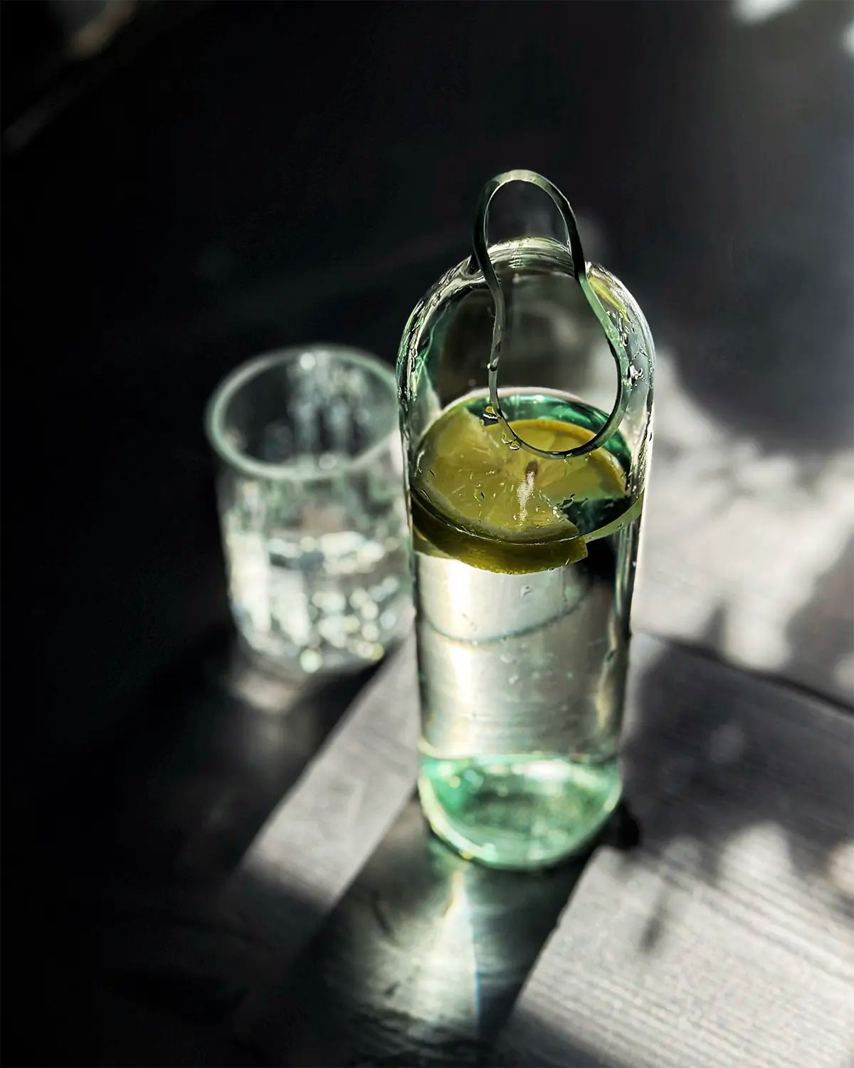 Glaskaraffe mit tropfenförmigem Ausguss aus einer geschliffenen Weinflasche mit Zitronenwasser und passendem Wasserglas