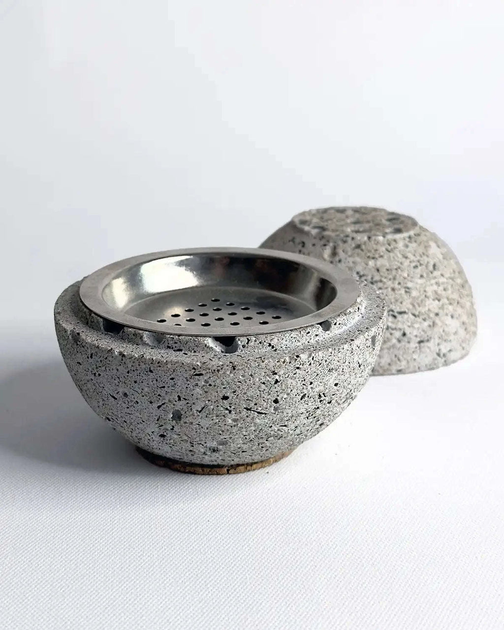 Geöffnete Räucherkugel Zazar aus grauem Beton mit sichtbarem Innenraum auf rauem Untergrund.