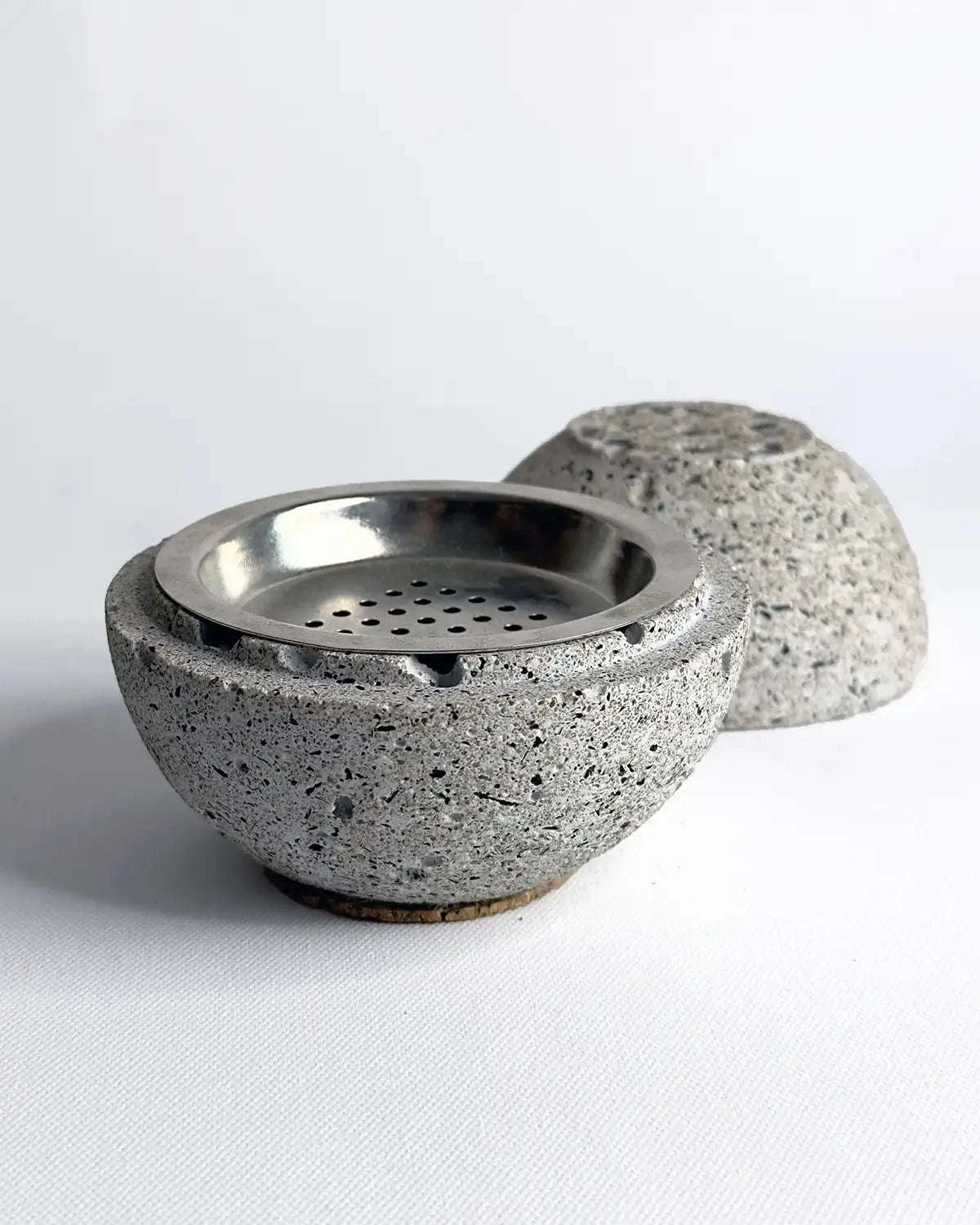 Geöffnete Räucherkugel Zazar aus grauem Beton mit sichtbarem Innenraum auf rauem Untergrund.